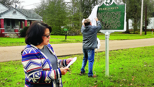 Photo by Josh Rich / Tammie Brewer (left) reads wording from the Pearlhaven Historical Marker to the crowd while her husband, Dennis, removes the sign’s covering Wednesday morning. The sign reads, “In 1899, the Pearl River Lumber Company established the mill town of Pearlhaven. Pearlhaven was incorporated in 1901 with 310 residents, who elected a mayor, board of aldermen, and marshal the same year. The mill town included a hotel, three churches, a hospital, school and 235 employee houses, plus a standard gauge railroad. By 1903, the population grew to more than 1,000. When the company was sold in 1905, the mill property and houses were auctioned off, and Pearlhaven was annexed into Brookhaven in 1912.”
