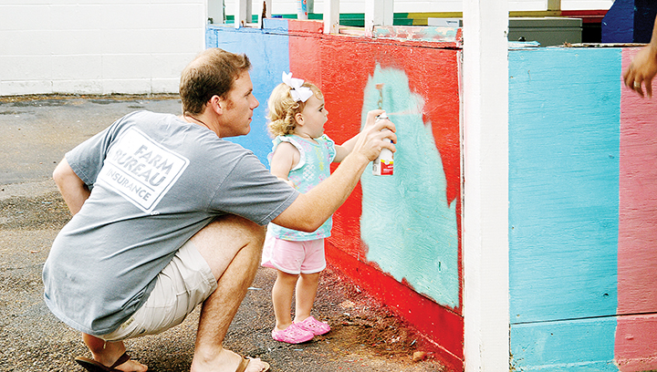 Photo by Donna Campbell/Eli Ferguson gets a little help painting from daughter, Maci, as members of the Brookhaven Exchange Club get the midway ready for the Exchange Club Fair, which starts Saturday. The fair, which the service club began in 1951, will run nightly from 6:30 to 10 p.m. through Aug. 6, except for Sunday when the fairgrounds is closed. There is free parking and free admission. Rides require the purchase of an armband, which is $10 for all ages and good for one day. Food and games will also be available. Proceeds from the fair are used to maintain Exchange Club Park and for scholarship and contributions to charitable organizations in the area. community through scholarships and donations to other charitable organizations.