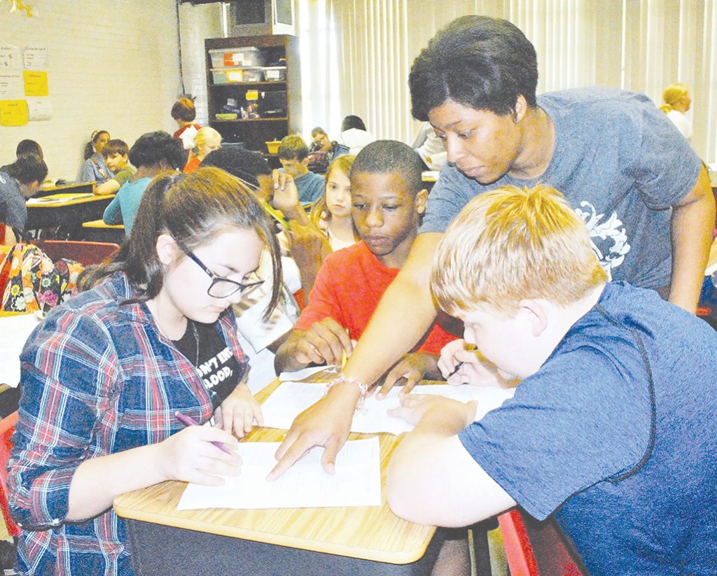 Photo by Aaron Paden/Sixth grade math teacher Shunta Davis helps a group of students with a decimals math project Thursday.