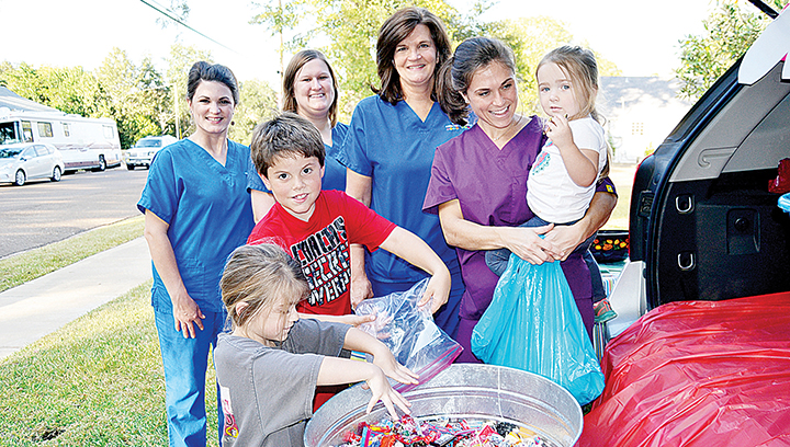 Photo by Donna Campbell/The staff of Ole Brook Pediatric Dentistry collected candy from trick-or-treaters the day after Halloween to send to troops overseas. Tossing some candy into the bucket are Charlotte Kilpatrick, 4, (left), and her brother, Elijah Kilpatrick, 8, who are surrounded by Brandi Leger, Michelle Nolan, Denise Thames and Dr. Joey Sessums, holding 3-year-old Cora Fuselier.
