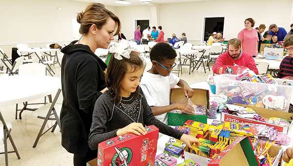 Photo by Donna Campbell/Angi Lins (left) helps Stella Lins and Kaleb Williams pack Operation Christmas Child boxes earlier this week. Aaron King and Cody Barrett, at the end of the table, mark the boxes with the appropriate stickers and seal them for travel.